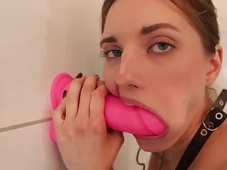 Nubile whore is deep throating a giant pink sex toy that's stuck to a wall